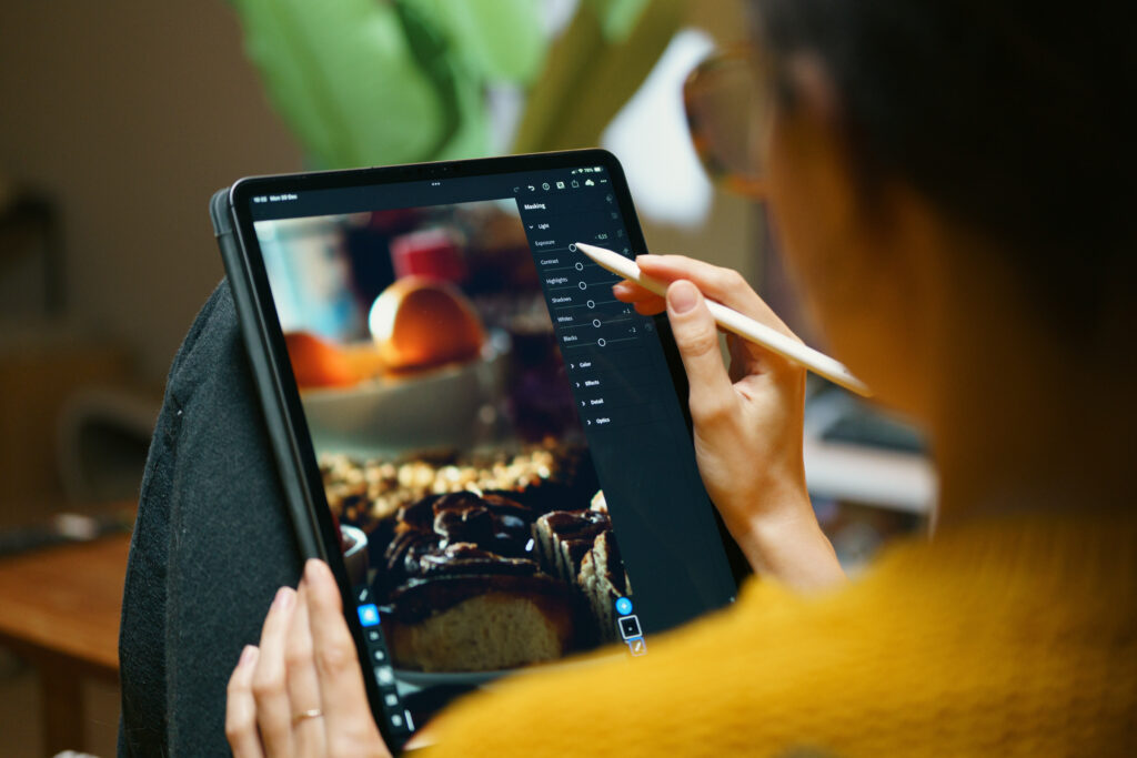 Frau, die ein Foto auf dem Tablet mit der Lightroom-Software und einem Stift bearbeitet, während sie sich zu Hause entspannt