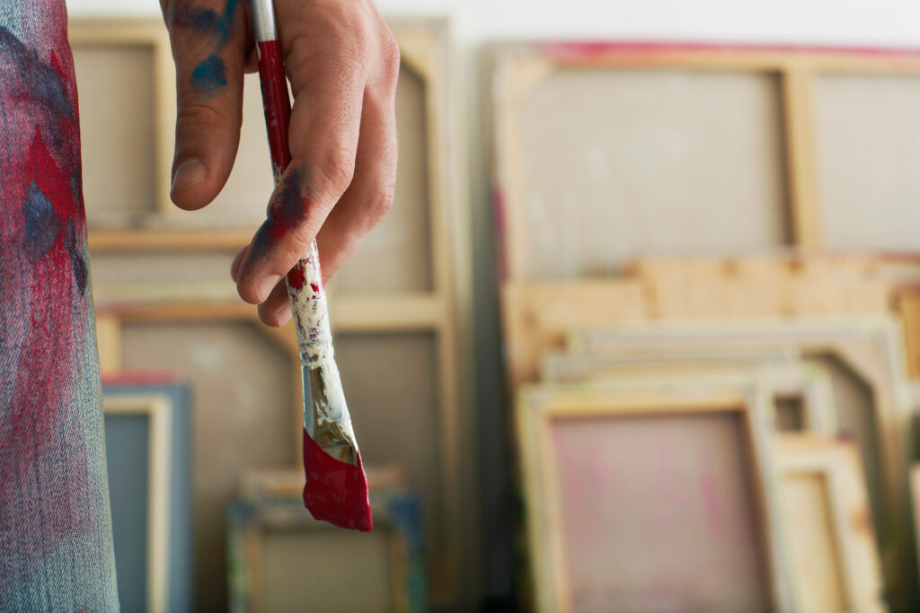 Closeup de um artista segurando um pincel com telas esticadas ao fundo