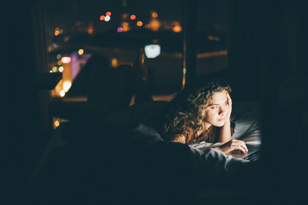 Woman is lying on the bed and using laptop computer at hotel room in the dark at the night.