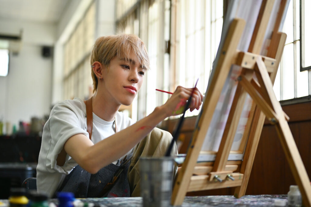 Portrait image of LGBT artist, an Asian teenager with colored hair doing artwork on an easel in a studio