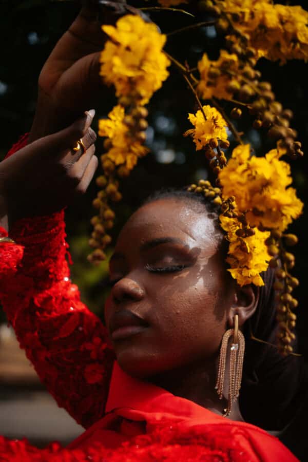 portrait rapproché d'une femme en robe rouge tenant des fleurs jaunes au-dessus de sa tête et portant des fleurs jaunes dans ses cheveux