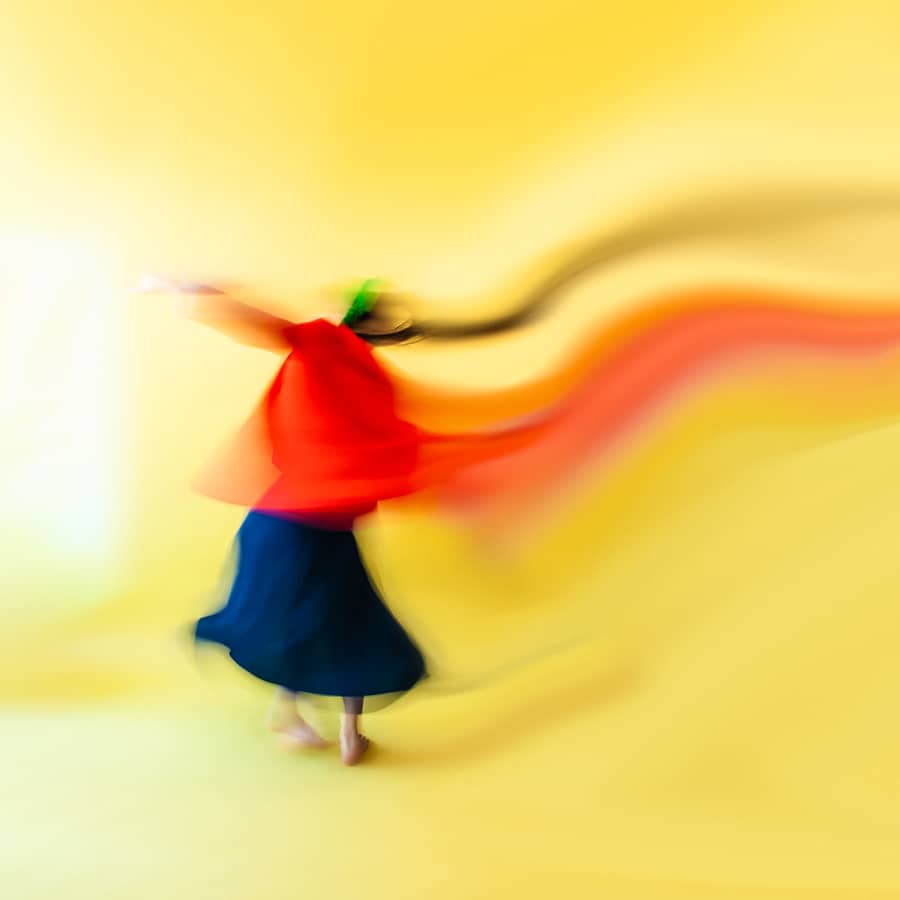 long exposure image of person wearing dark blue and red dancing across a yellow backdrop. Titled Dance II n°28 by Émilie Möri