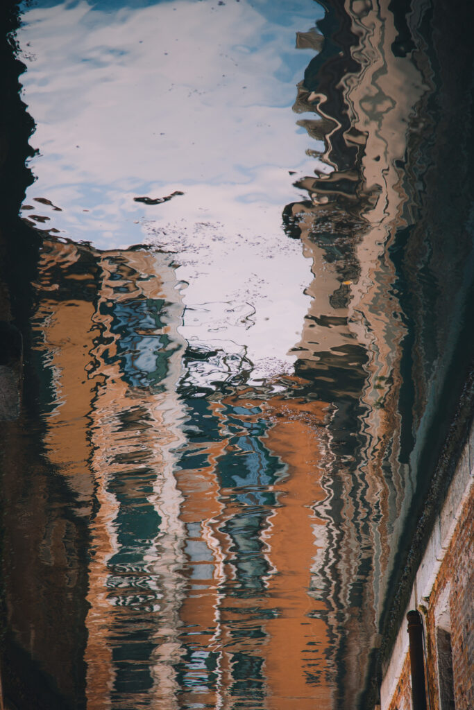 photograph of a rippled reflection of rust and brown buildings in water by Mayank Thammalla