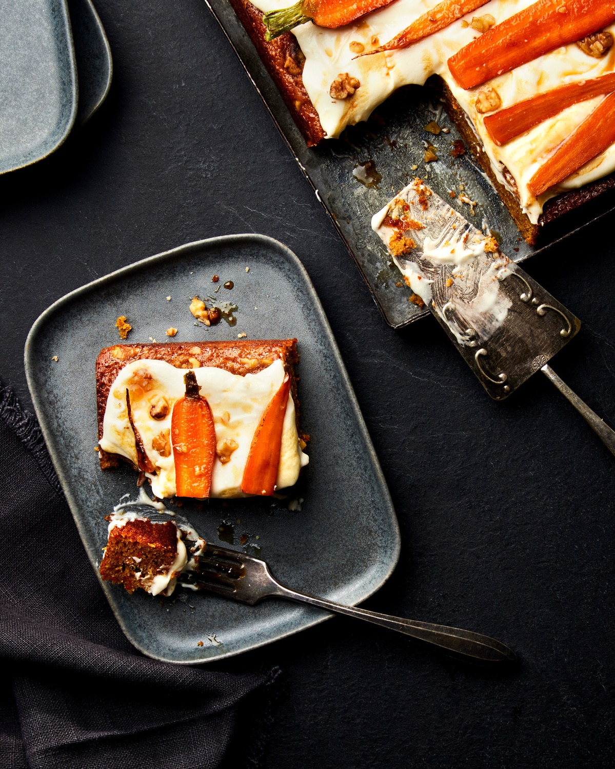 photo of carrot cake topped with glazed carrots on a dark grey plate by Dan Robb