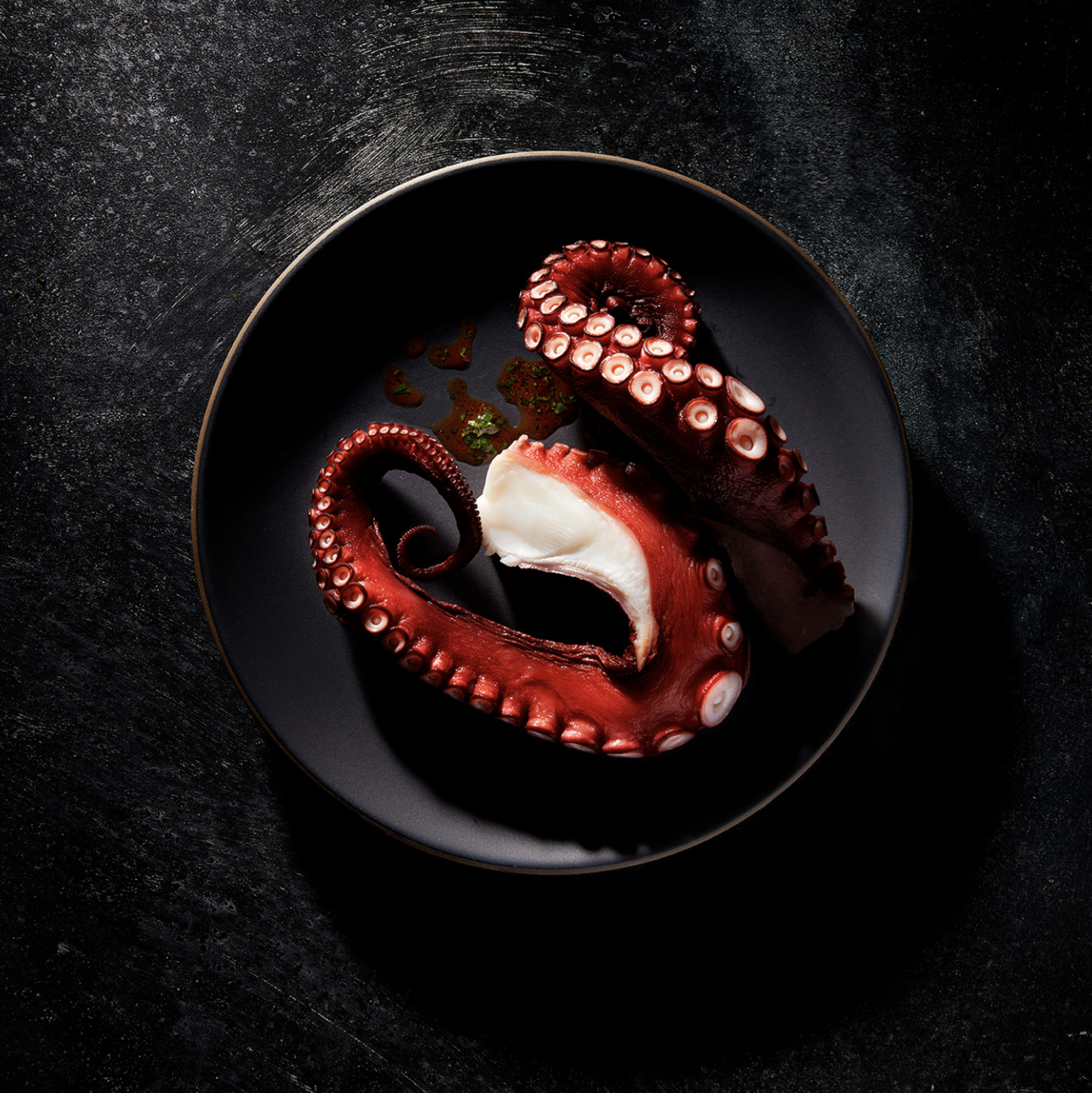 photo of crimson and white squid tentacles on a black plate by Nadim Sabella