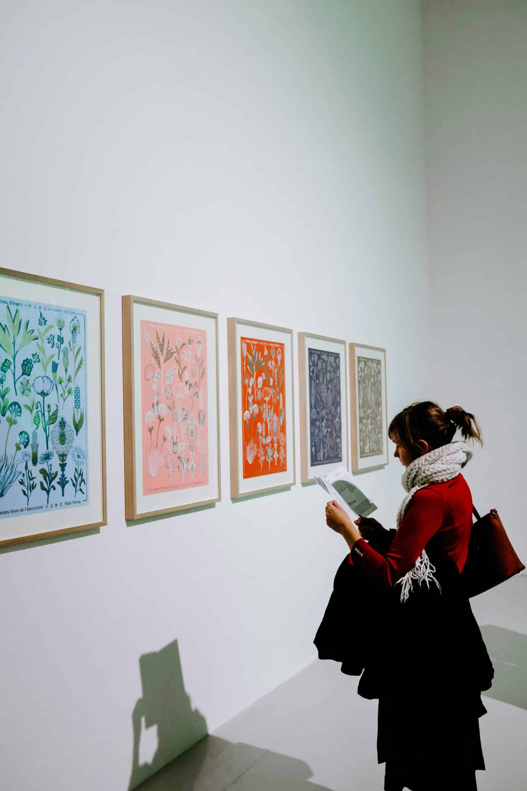 woman standing in front of a series of paintings on a white wall