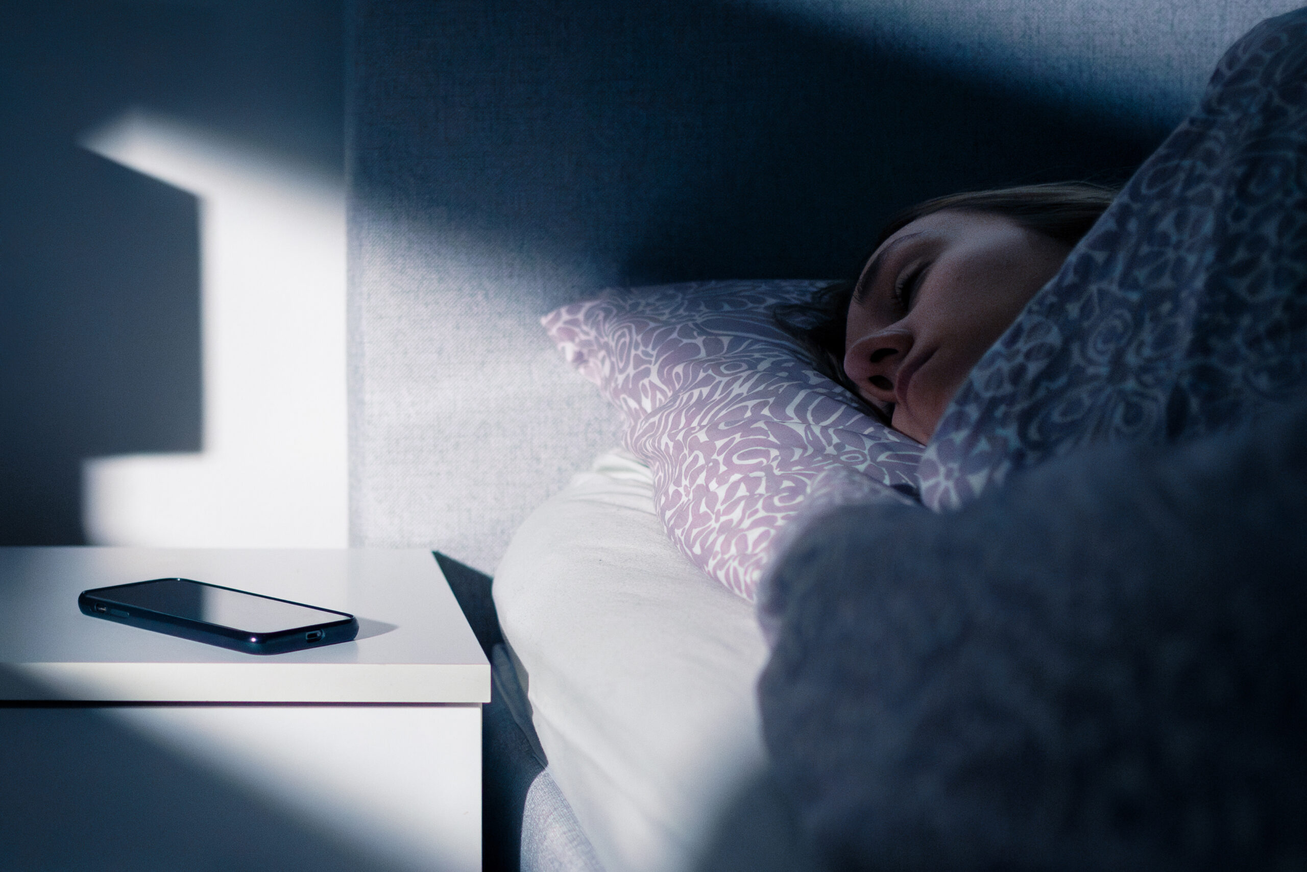 Phone on nightstand next to bed while person is sleeping.