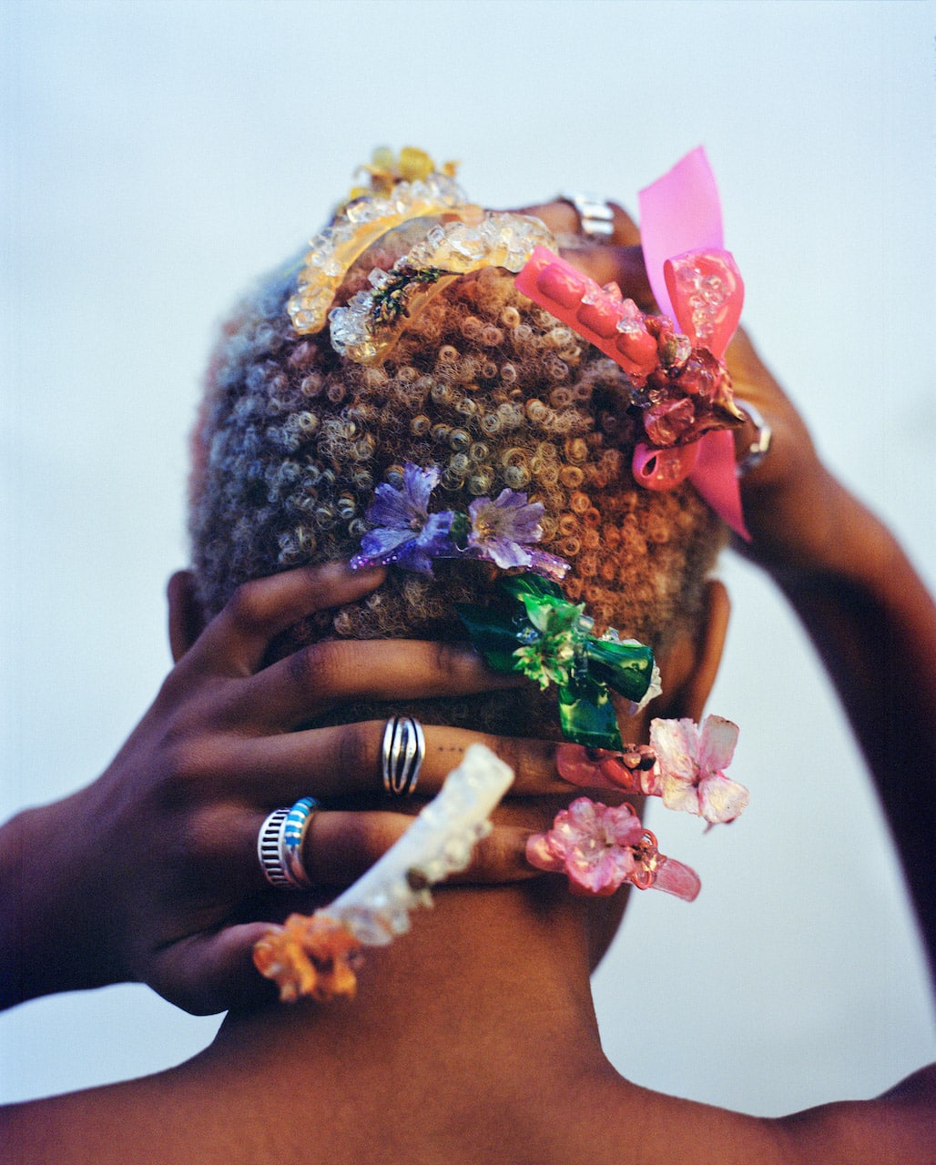 black woman's head with very short, bleached blond curls, partially covered by her hands and colorfully decorated 3 inch fingernails. photo by JANNELL ADUFO