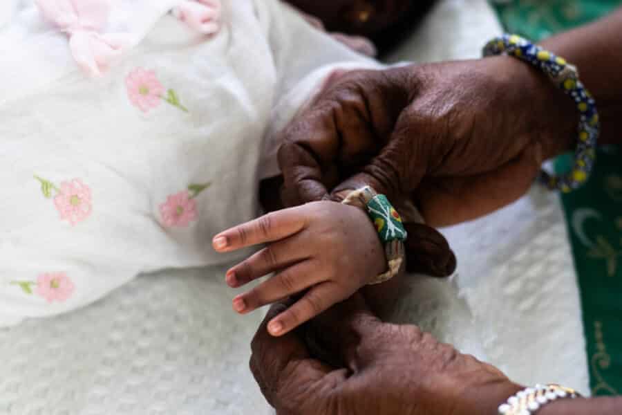 Mãos femininas enrugadas pela idade colocando uma pulseira no pulso de um bebê