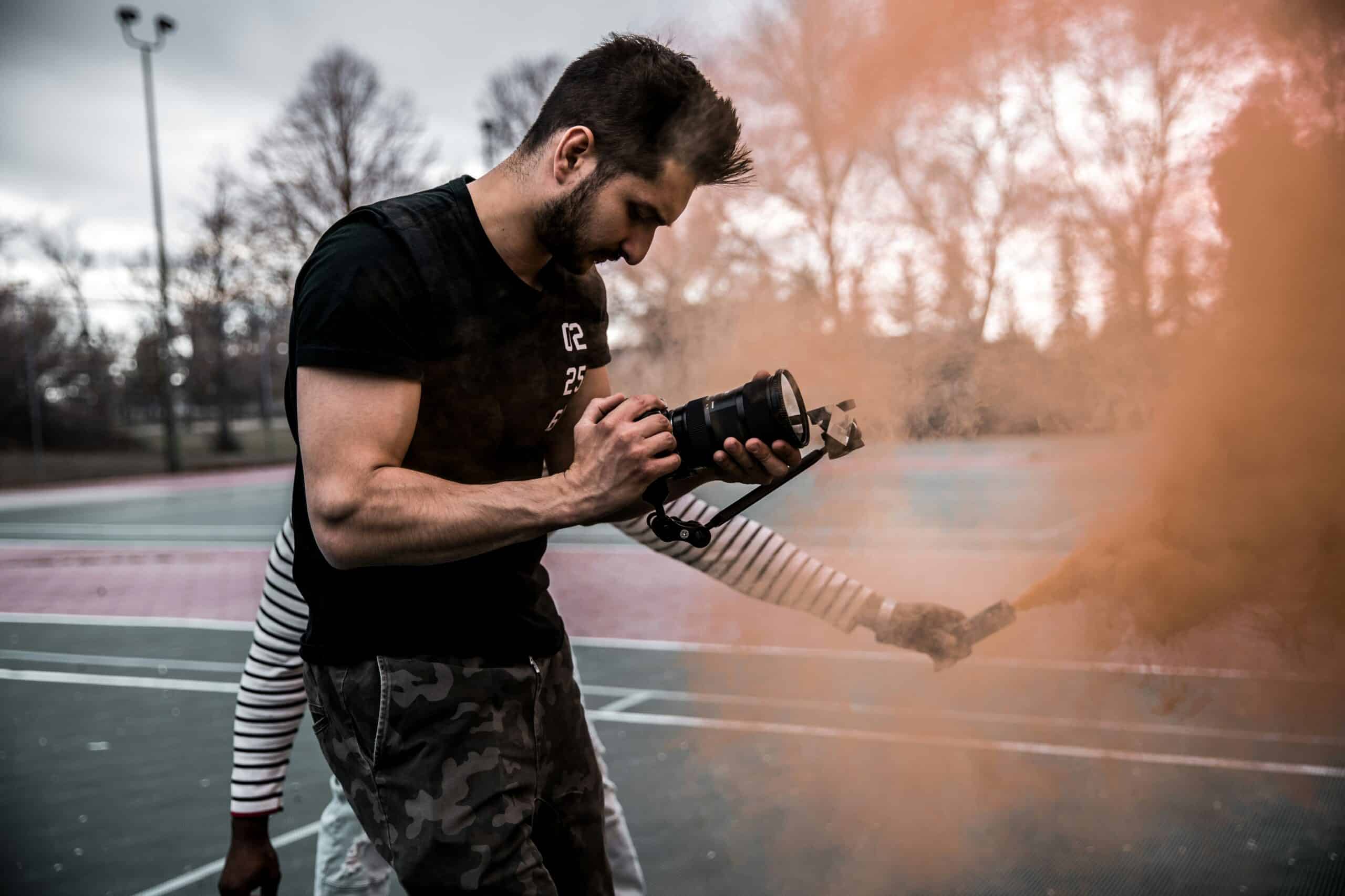 Photographer on outdoor shoot aiming camera through colored smoke scaled