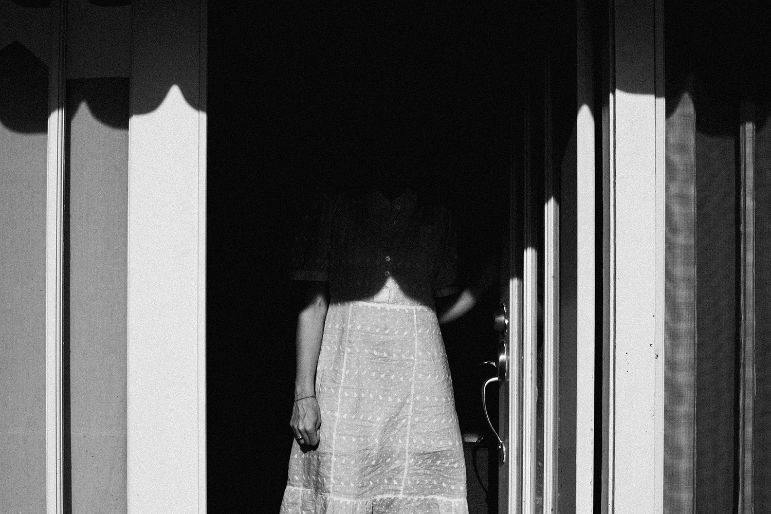 figure of a woman standing in a doorway, top half of her body hidden by shadows. photo by TJ Martin