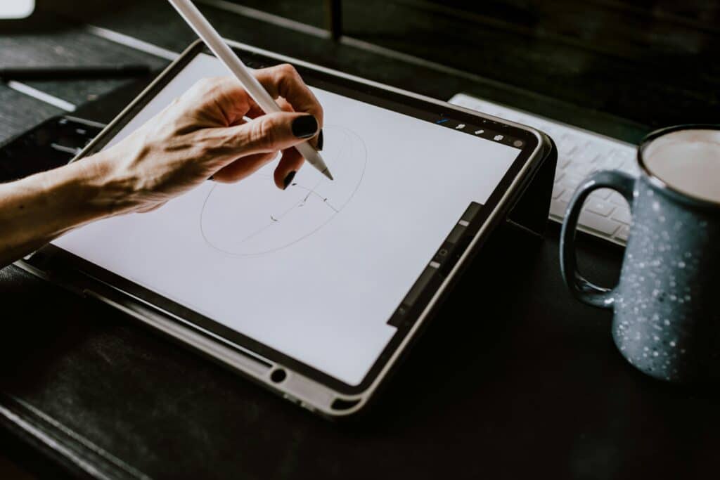 Mãos de mulher desenhando em um iPad ao lado de uma xícara de café texturizada