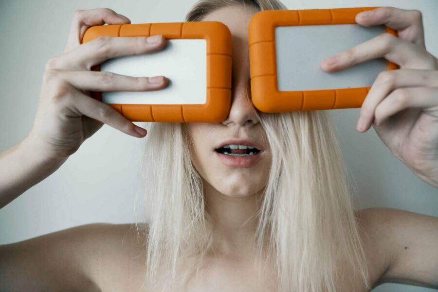 femme blonde tenant deux disques durs orange et argent au-dessus de ses yeux échelle e1715794105421