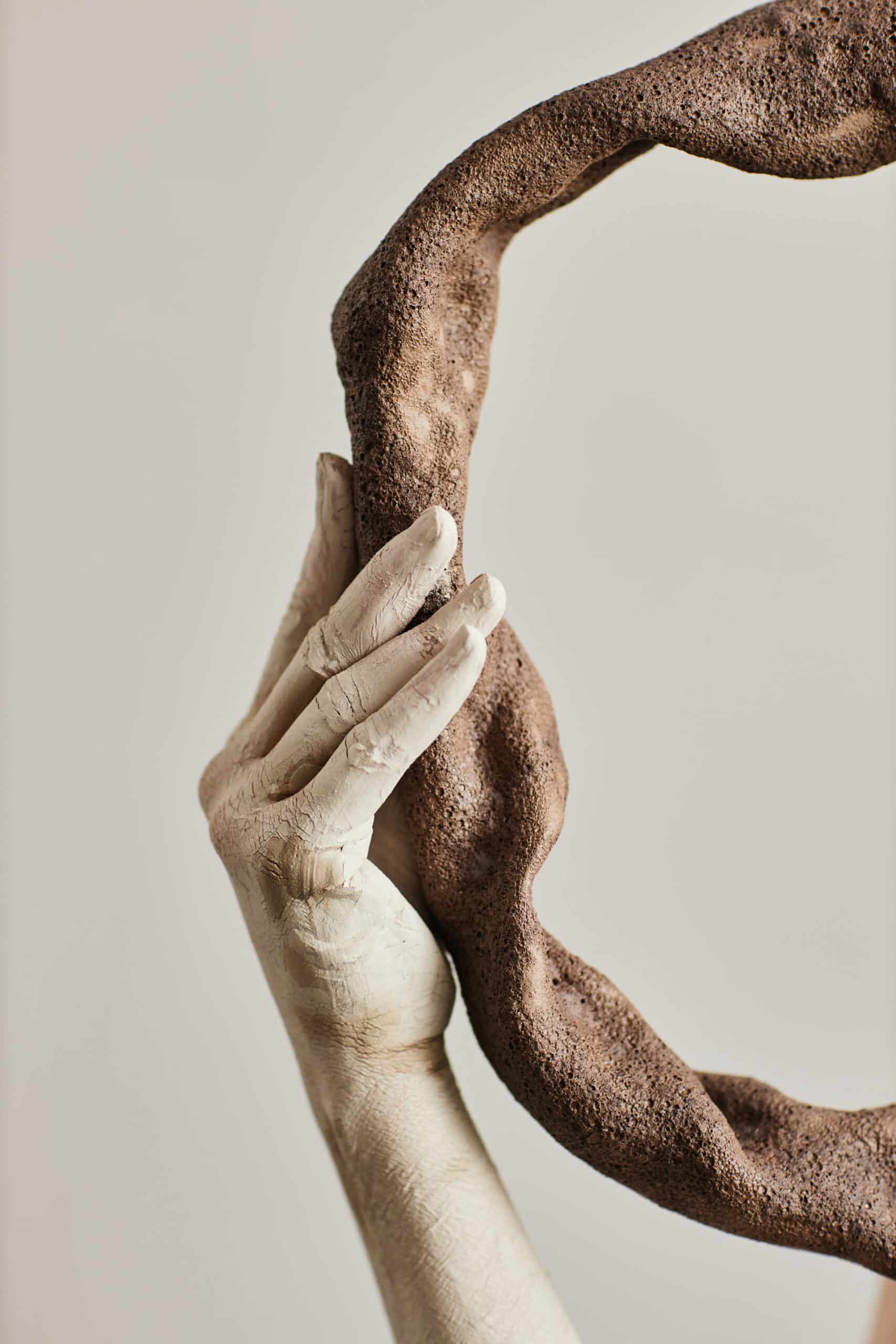 Close up of hand covered in plaster holding ceramic art piece minimal