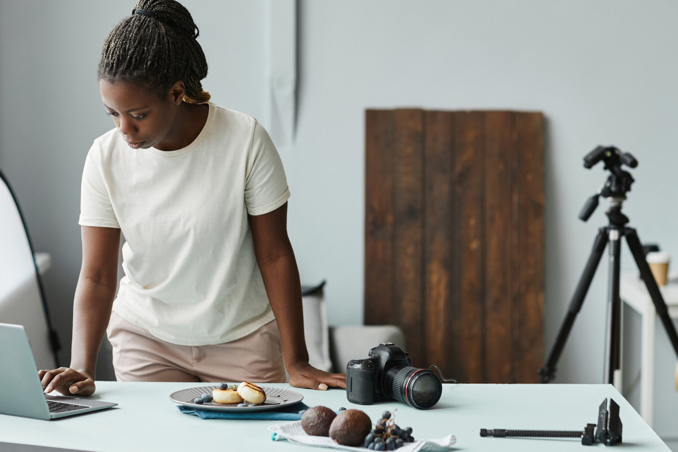 Porträt einer jungen afroamerikanischen Frau, die einen Laptop benutzt, während sie im Studio mit Lebensmittelfotografie arbeitet