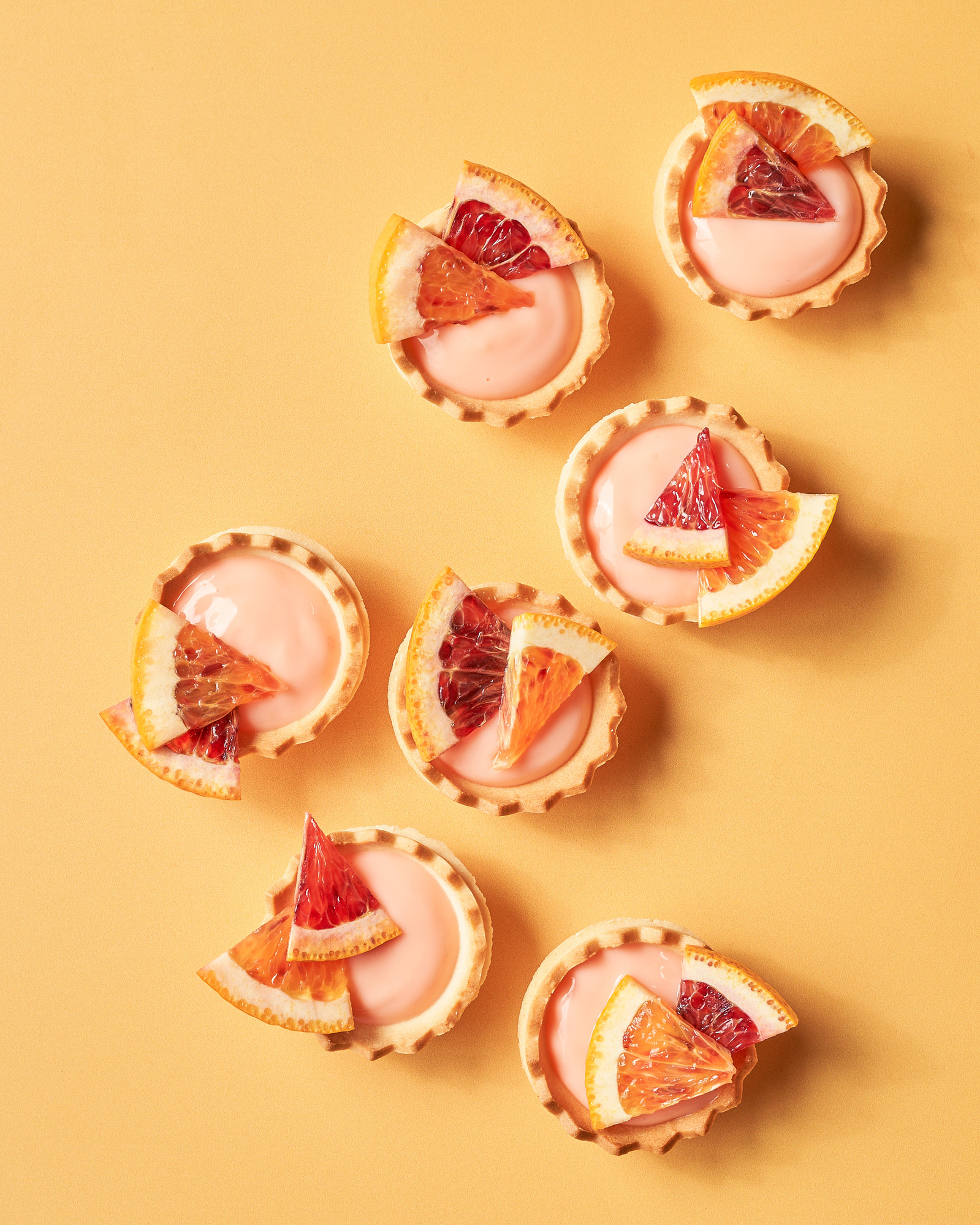 photo of tiny pink tarts topped with blood orange segments on a pale orange surface by hilaire baumgartner