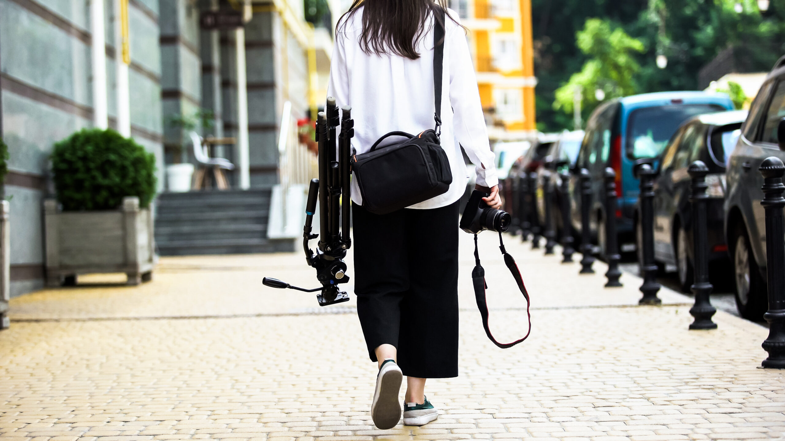 photographer walking down sidewalk with tripod and camera