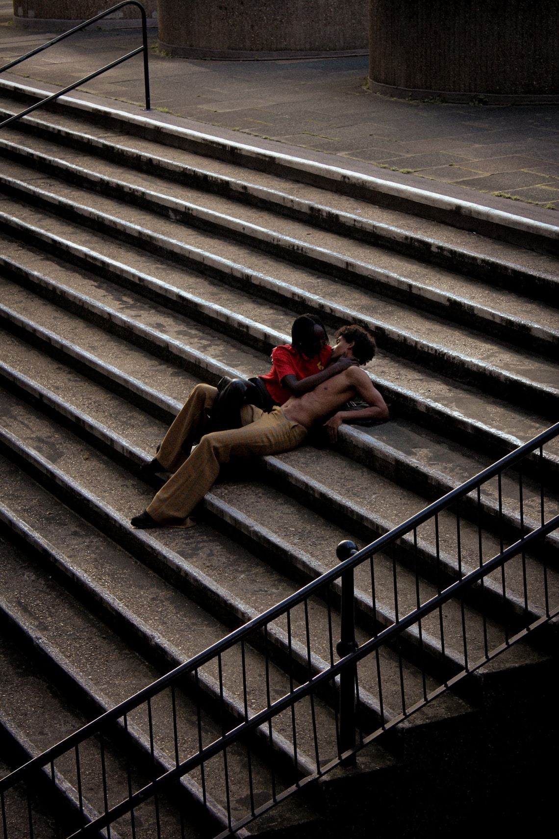 two figures resting casually and intimately together on cement stairs. photo by riac oseph