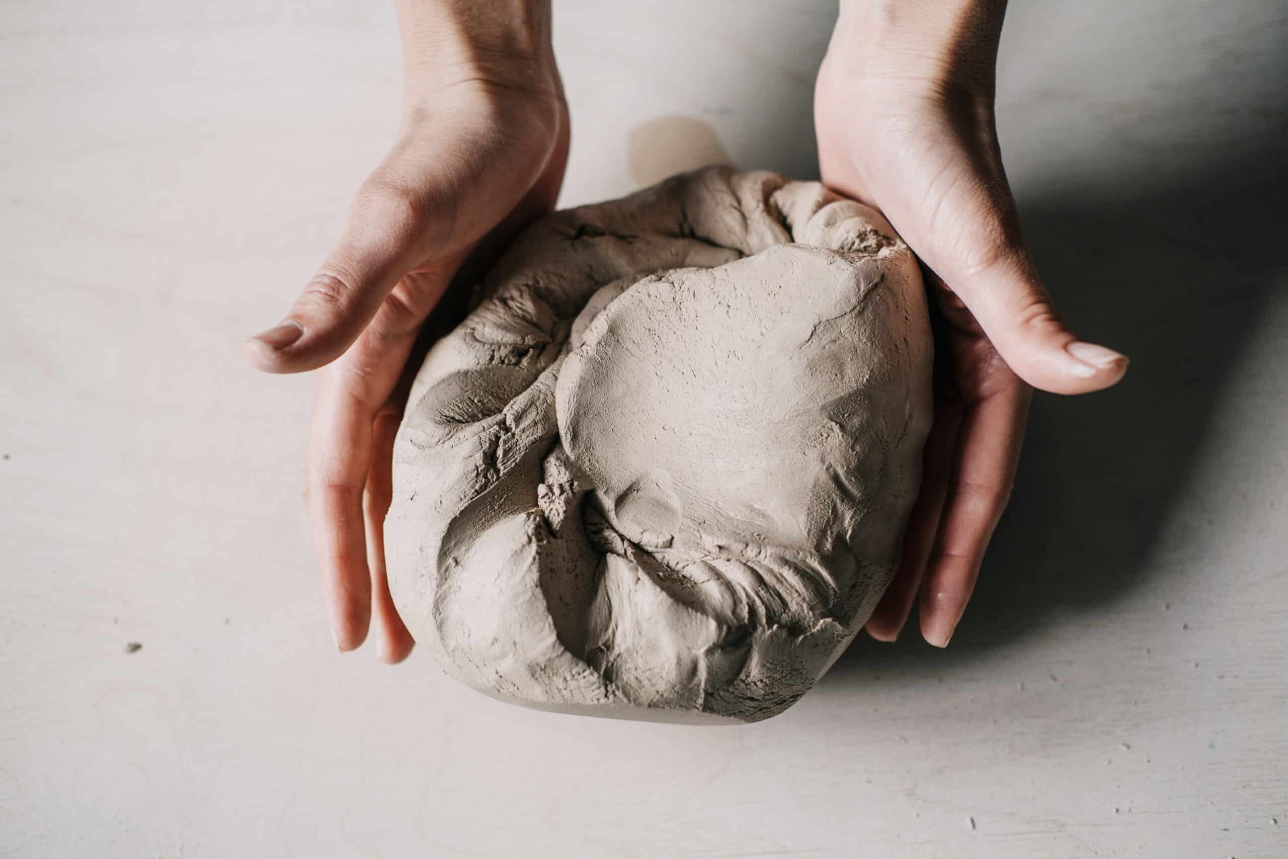 Female potter hands holding kneaded clay in workshop.