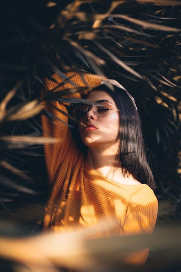 woman in yellow shirt and orange makeup posing between spiky leaves scaled e1682611281621